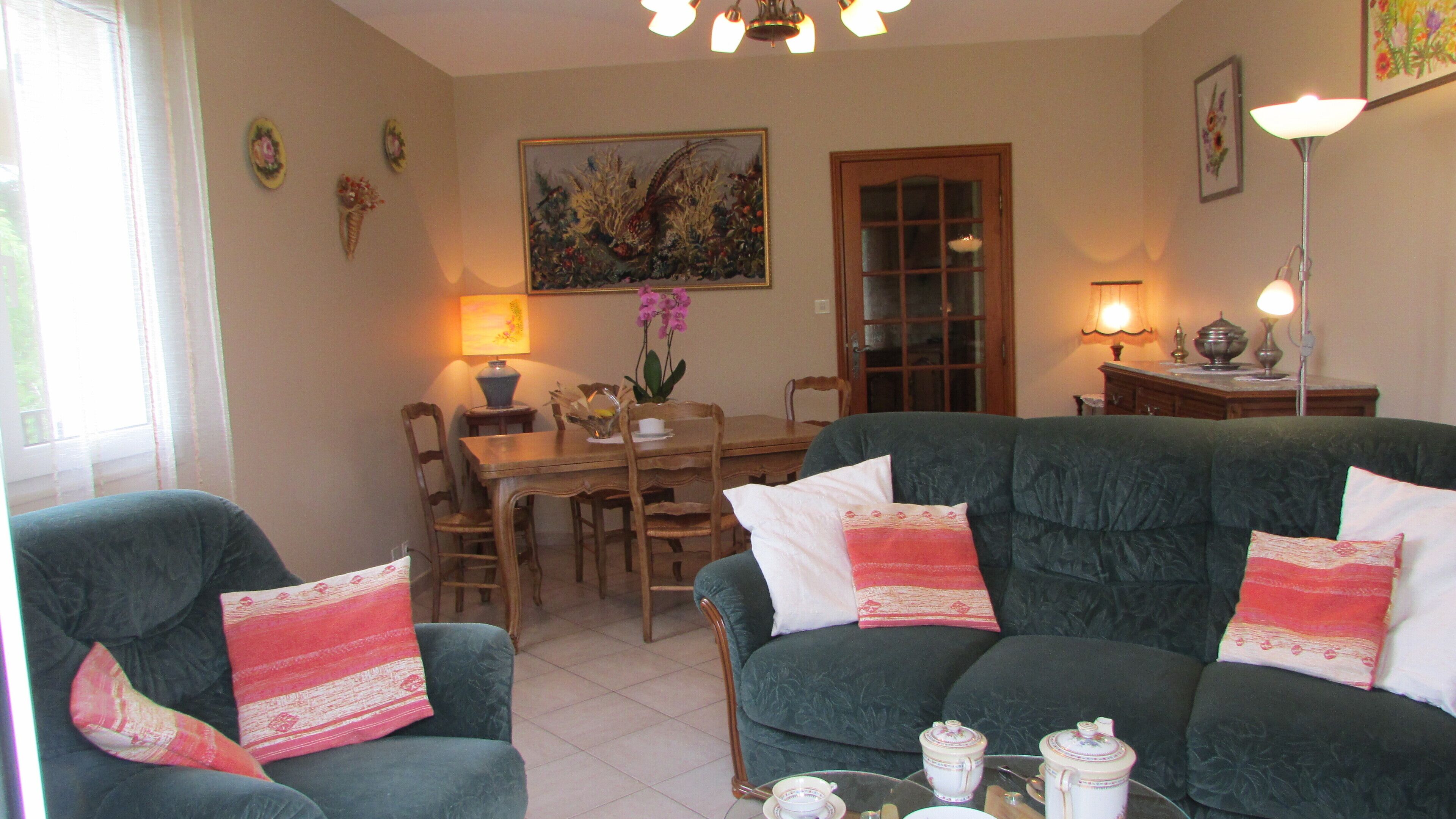 A living room with a green sofa, a dining table, chairs, and a painting on the wall.
