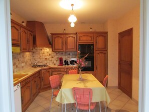Une cuisine avec des meubles de rangement en bois, un pare-feu en carrelage, une cuisinière à gaz, un four à micro-ondes et une table à manger avec des chaises.