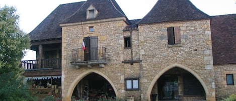 Un bâtiment en pierre doté de deux entrées en arc de cercle, d’un balcon avec une balustrade et d’un drapeau.