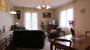 Un salon avec un canapé, une table à manger et des chaises, un téléviseur, une plante et une lampe.