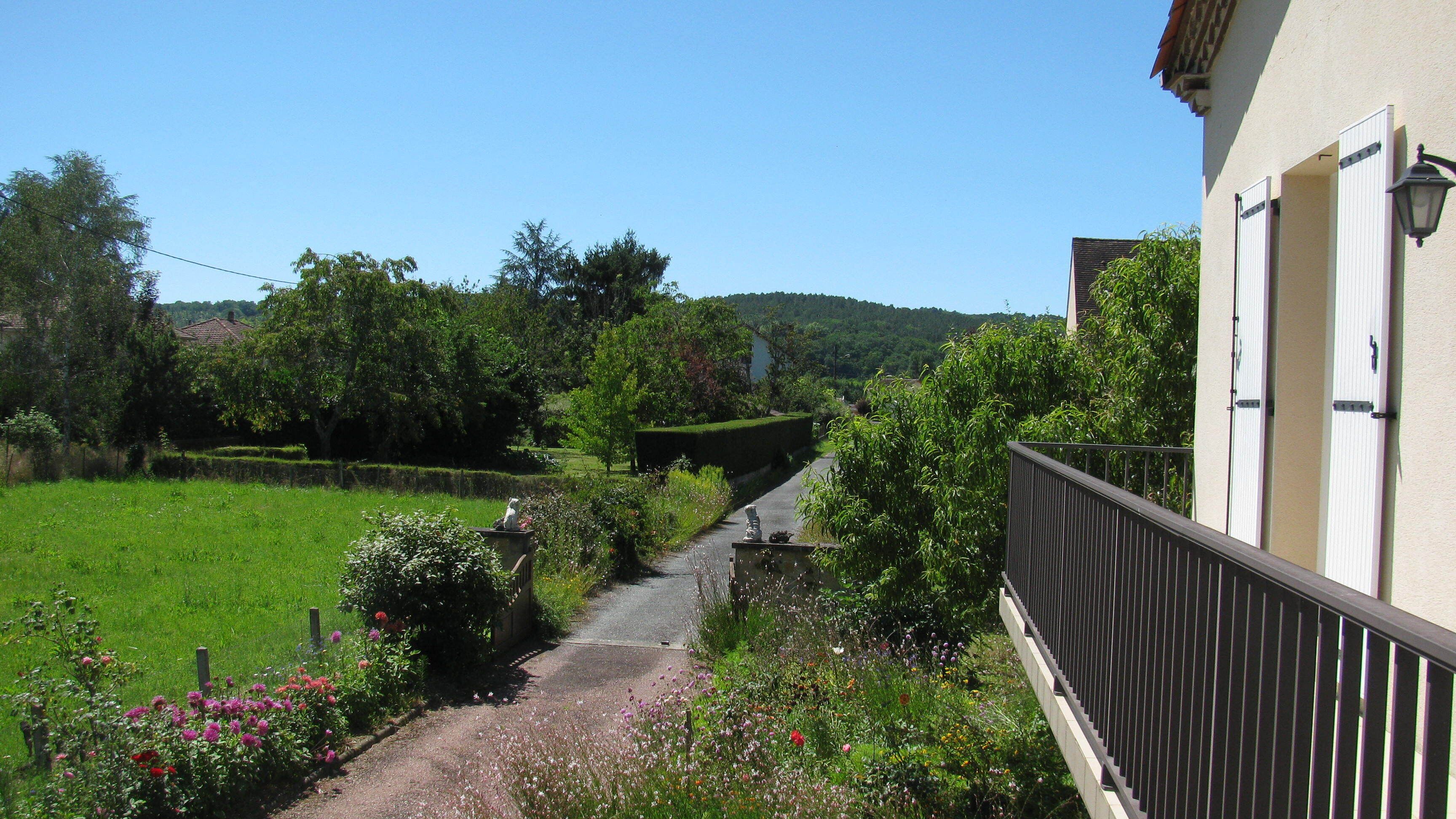 A pathway leading to a building with a balcony, surrounded by lush greenery and a well-maintained garden.