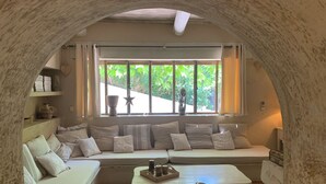 Ein gemütliches Zimmer mit eingebauter Bank und kleinem Tisch, einem fenster mit Vorhängen und Blick auf Grünflächen.