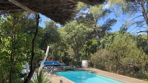 Ein Poolbereich mit Holzterrasse, Liegestühlen und einer Struktur mit Reetdach.