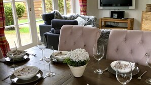 A dining area with a table set for two, a television, and a sofa in the background.