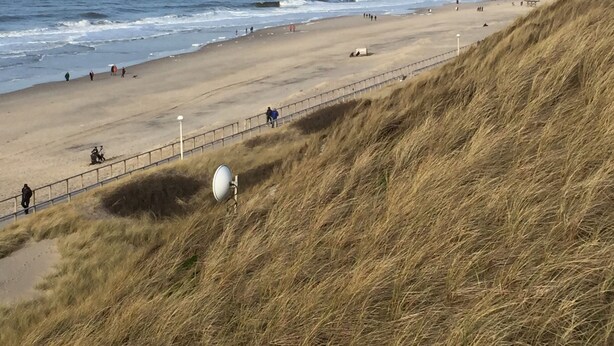 A beach with a sandy shore, a grassy dune, and the ocean in the background.