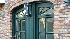 A dark green double door with a small window above it, set in a brick wall.