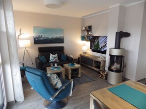 A modern living room with a sofa, a blue armchair, a coffee table, a TV, a fireplace, and a painting on the wall.