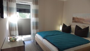 Een slaapkamer met een bed, een nachtkastje met een lamp, een raam met gordijnen en een schilderij aan de muur.