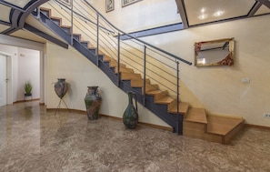 A staircase with a metal railing, a wall-mounted mirror, and three large vases on the floor.