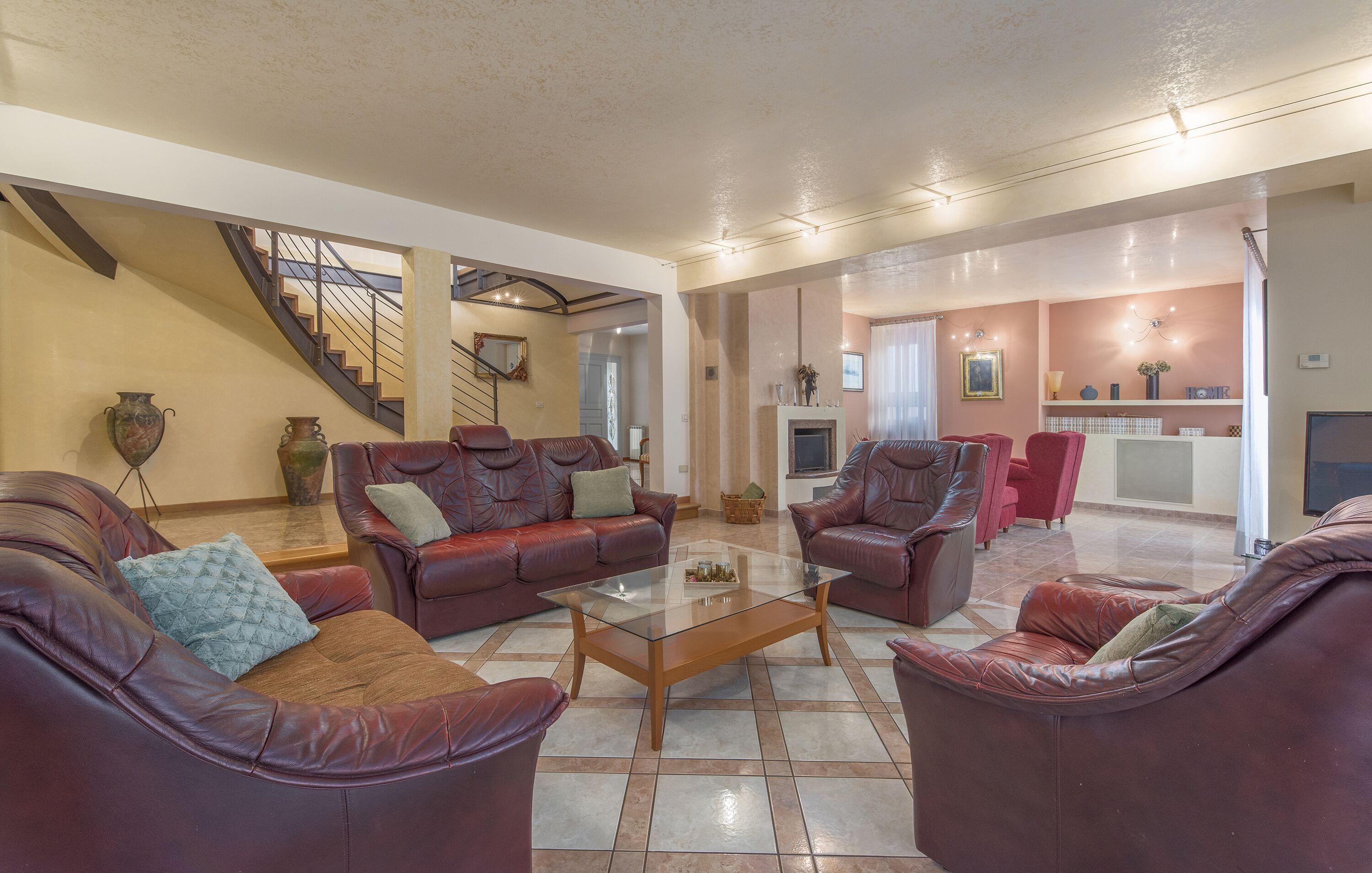A spacious living area with leather sofas, a glass coffee table, and a staircase leading to another level.