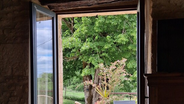 Une pièce donnant sur un jardin, avec un fauteuil en osier et une table surmontée d’un tapis à motifs.