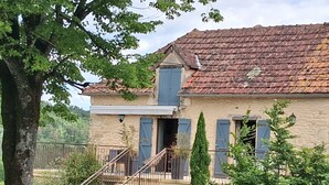Une maison en pierre à deux étages, avec un toit en tuiles, un escalier menant à l’entrée et un jardin clos.