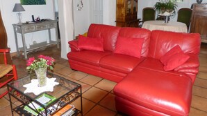 Un salon avec un canapé en cuir rouge, une table basse en verre sur laquelle sont posés des livres, un meuble en bois et un tableau accroché au mur.