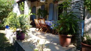 Un bâtiment en pierre doté d’un patio couvert, de sièges en plein air et de plantes en pot.