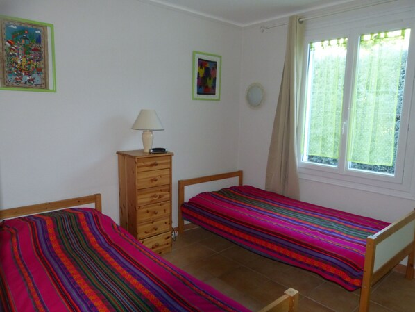 A bedroom with two single beds, a wooden dresser, a lamp, and a window with curtains. - * September sale * Comfortable villa, 1300 m2 of fenced and wooded land (Cheval-Blanc)
