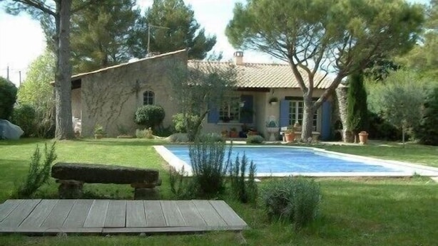 Une maison en pierre avec une piscine, entourée d’arbres et d’une pelouse verdoyante.