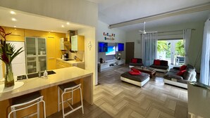 A modern living room with a sofa set, a coffee table, and a TV. There is a kitchen area with a counter and stools. - BEAUTIFUL COUNTRY PROPERTY WITH PRIVATE POOL. HOLIDAYS TO YOU! (SAINTE ANNE)