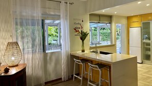 A modern kitchen with a central island, white bar stools, a large window with curtains, and a decorative wall sign. - BEAUTIFUL COUNTRY PROPERTY WITH PRIVATE POOL. HOLIDAYS TO YOU! (SAINTE ANNE)