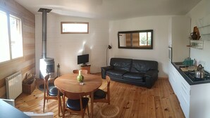 Una sala de estar acogedora con chimenea, un sofá de cuero negro, una mesa de comedor de madera con sillas y una zona de cocina con estufa.