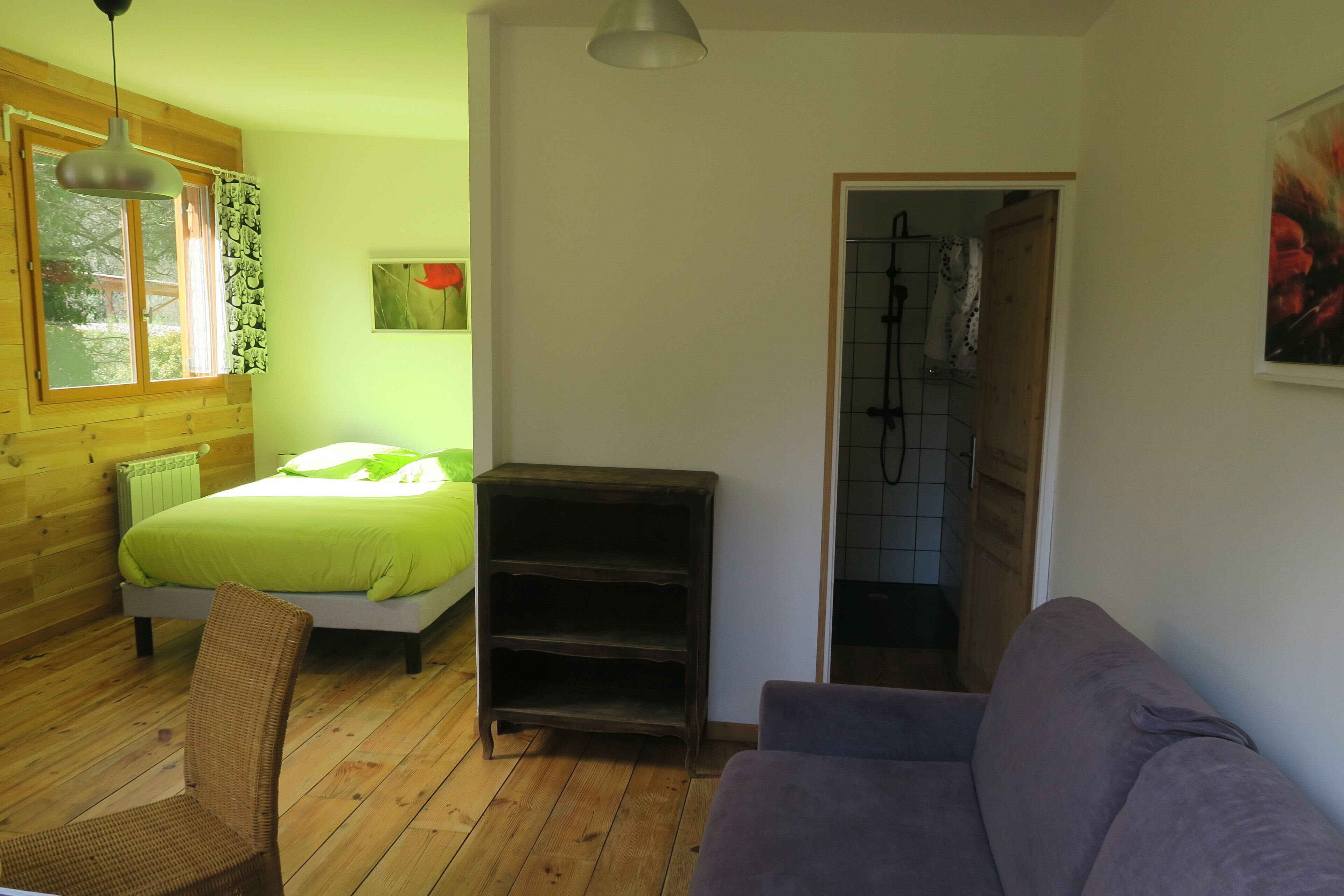 Een kamer met een bed, een stoel, een bank, een plank en een raam met gordijnen.