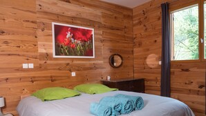Una habitación con paneles de madera, una cama, almohadas verdes, una toalla azul, un cuadro enmarcado y un espejo.