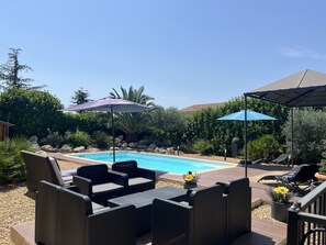 Un espace piscine agrémenté de chaises longues et de parasols, entouré de verdure et de rochers.
