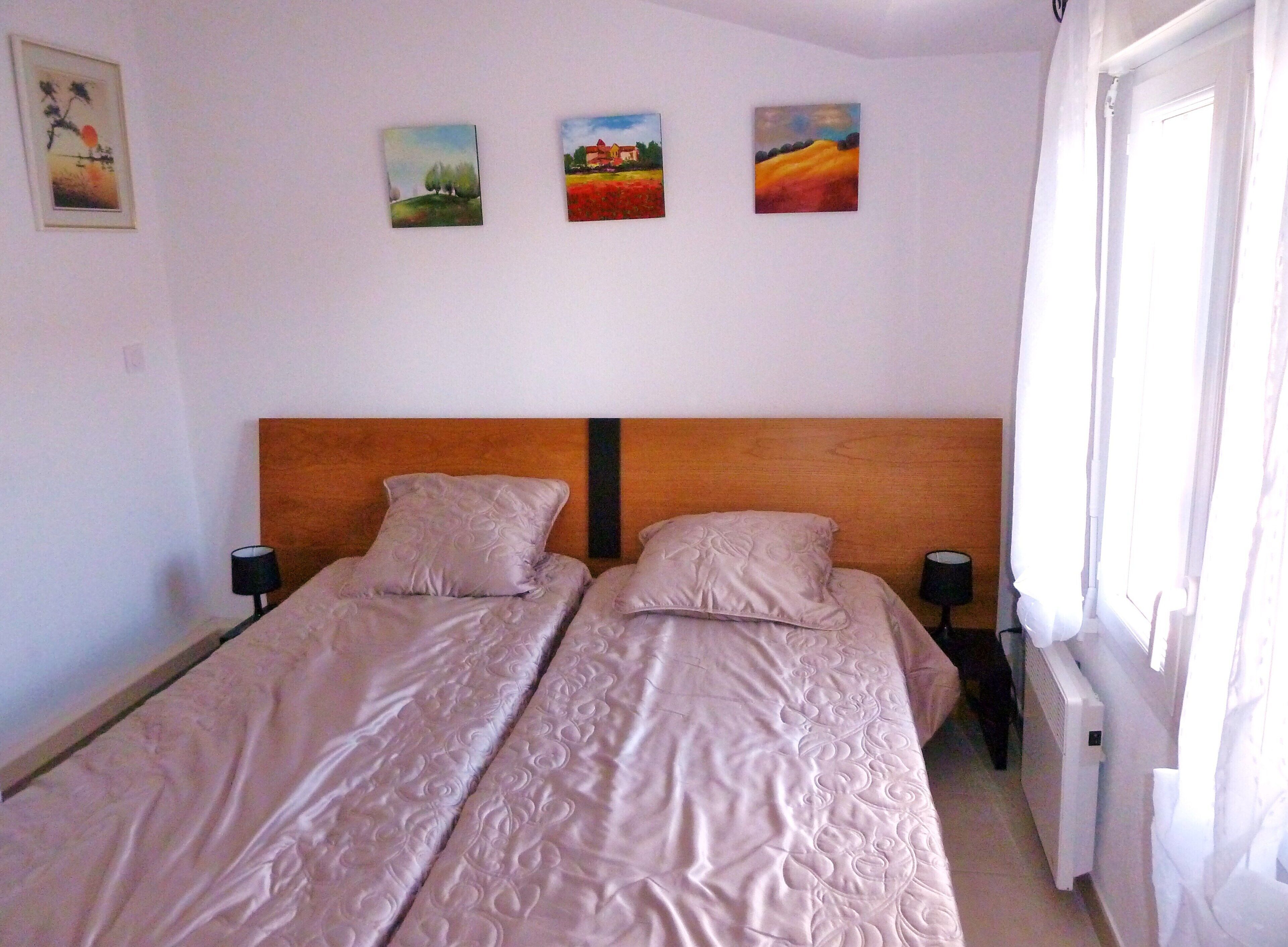 A double bed with a wooden headboard, two bedside tables, and three paintings on the wall.