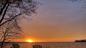 Auringonlaskunäkymä, jossa on kaksi puista tuolia, ja ne ovat käännettyjä kohti tyyntä vesialuetta.