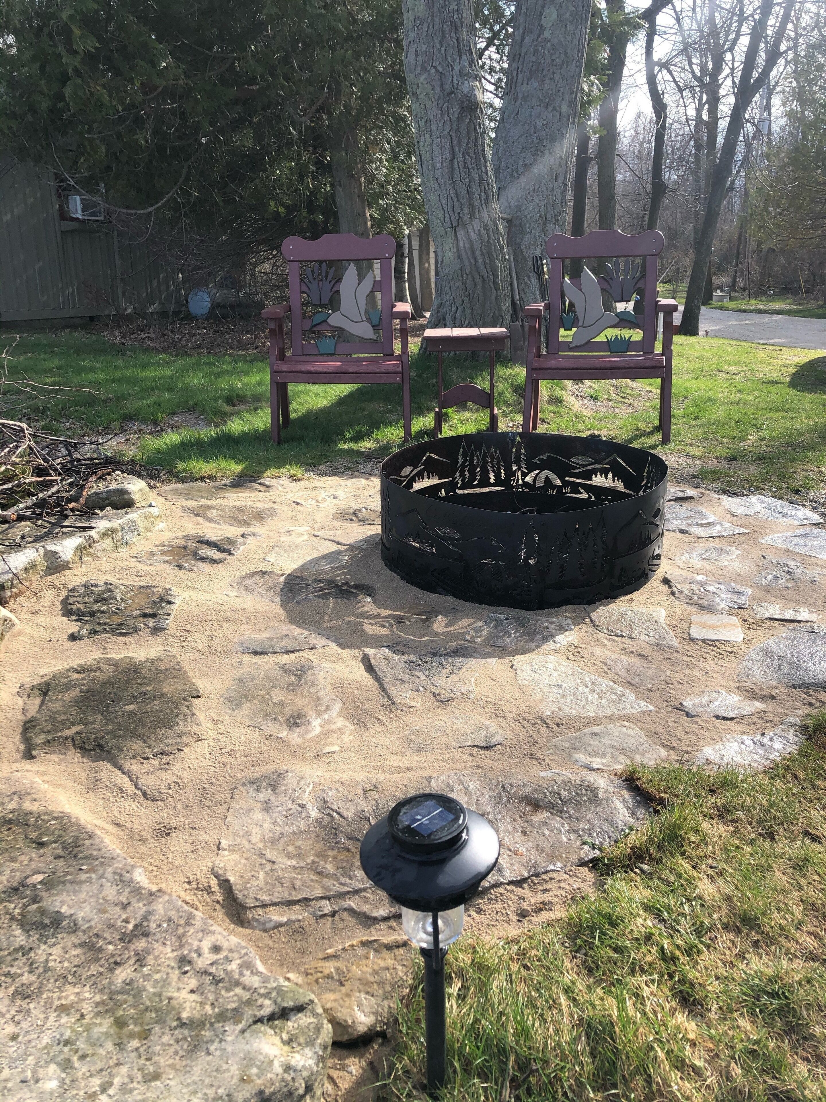 A stone fire pit with a lantern in the foreground, surrounded by grass and rocks.