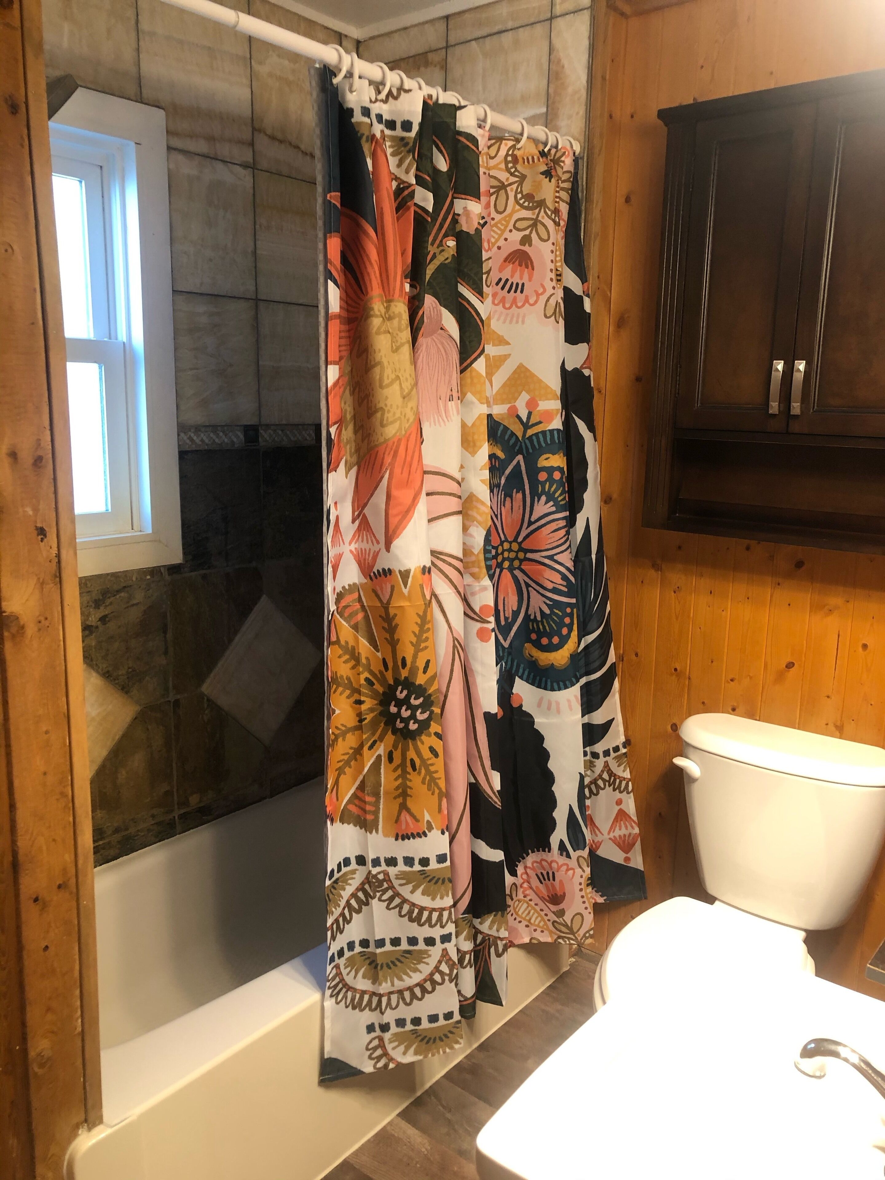 Um banheiro com cortina de chuveiro estampada com padrão floral, vaso sanitário branco e painéis de madeira nas paredes.
