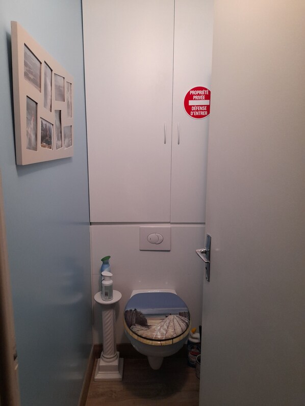 Une salle de bain avec des toilettes, un petit lavabo et un meuble. Il y a un panneau rouge sur le mur et un cadre photo sur la gauche.