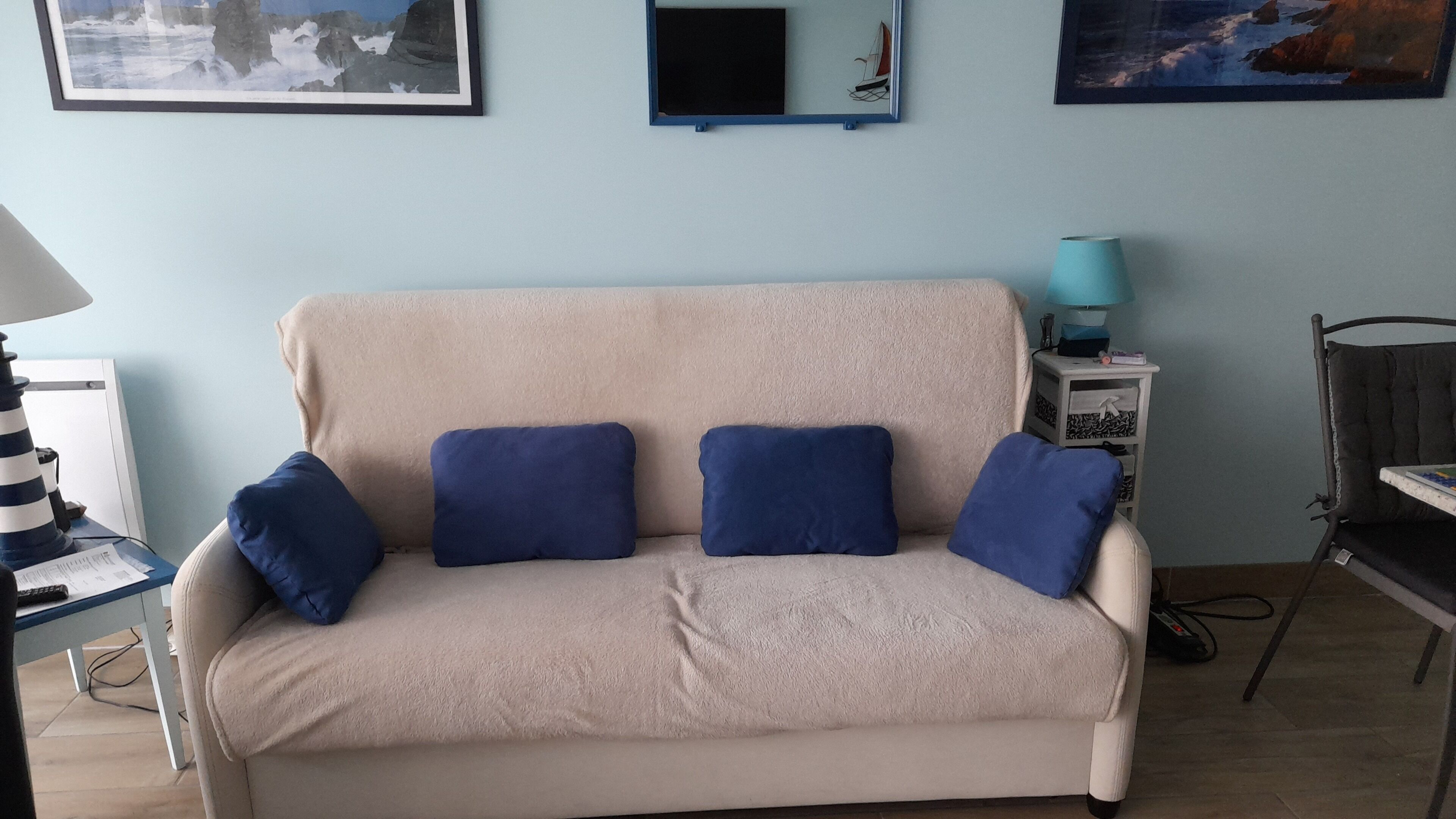 A beige sofa with four blue cushions, a small table with a lamp, and a framed picture on the wall.