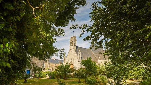 Une église entourée d’une végétation luxuriante et traversée par un petit ruisseau.
