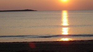 Un coucher de soleil sur une mer calme, avec une terre lointaine à l'horizon.