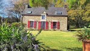 Une maison en pierre avec des volets rouges, un petit balcon et un jardin bien entretenu.
