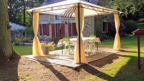 Un espace extérieur abrité, aménagé avec une table et des chaises, un pot de fleurs et une nichoir.