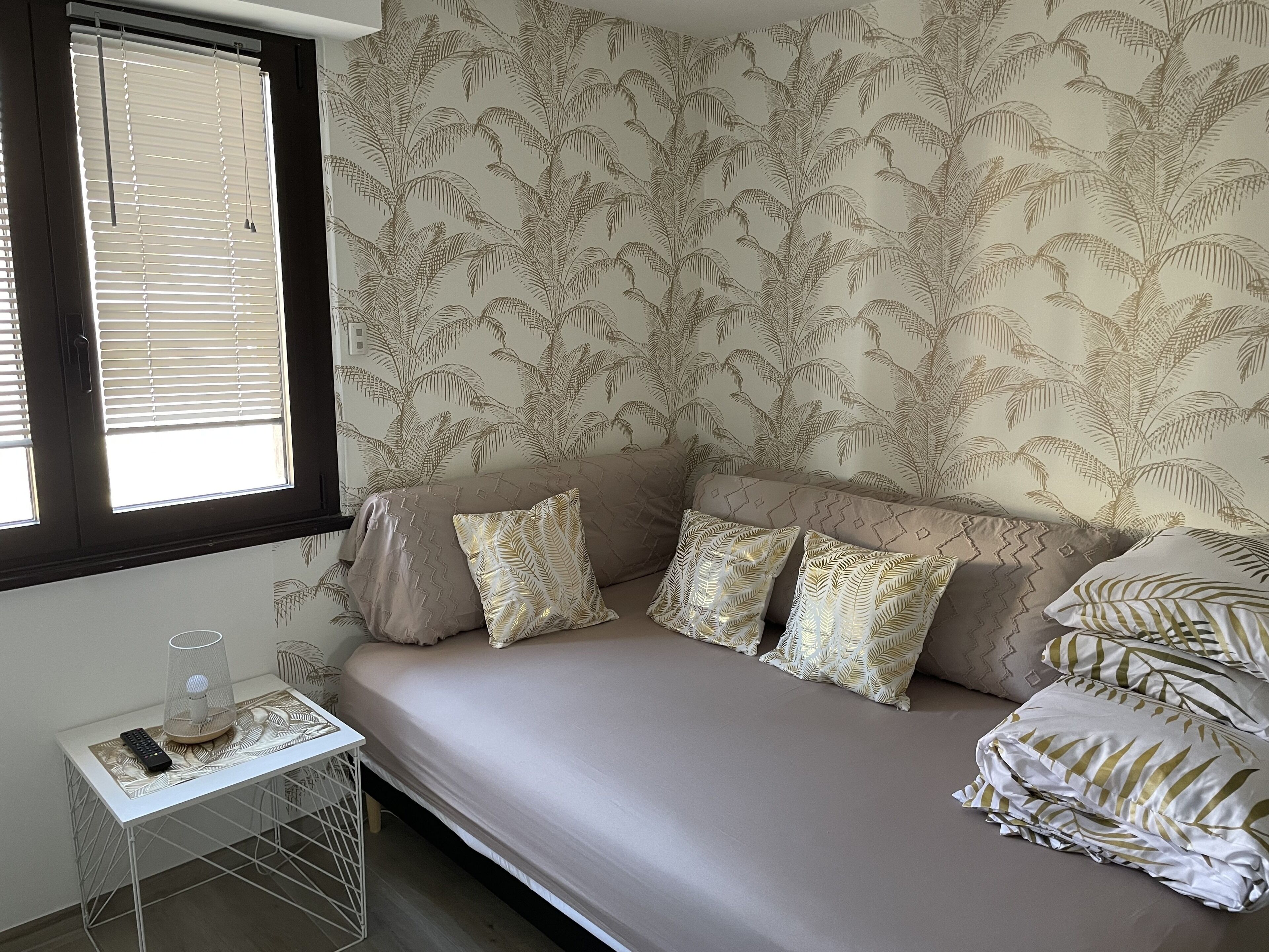 A room with a sofa, patterned cushions, a small table with a lamp, and a window with blinds.