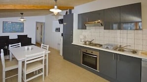 Una cocina compacta con armarios oscuros, una encimera blanca y una zona de comedor con una mesa y sillas blancas.