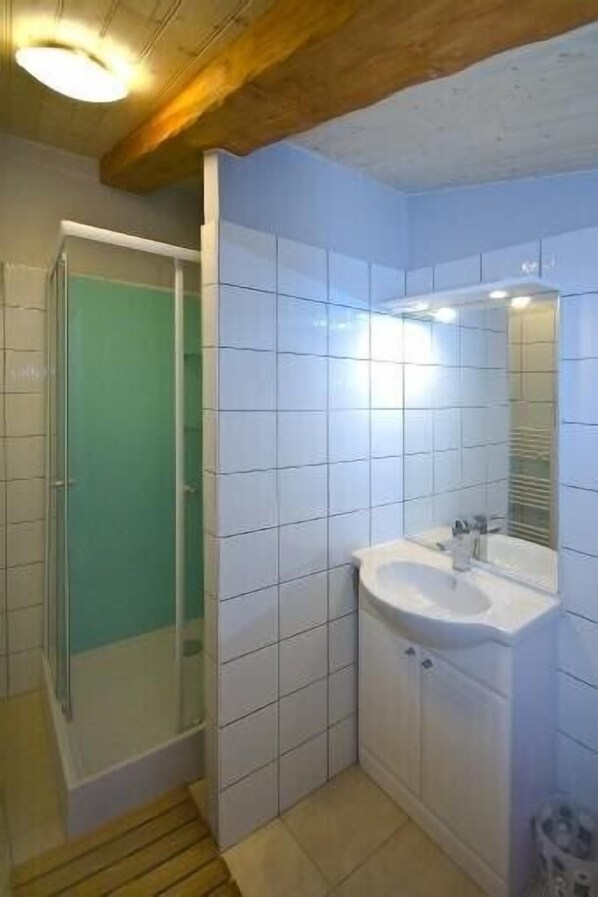 A bathroom with white tiles, a sink, a mirror, and a shower enclosure.