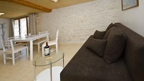 Una sala de estar con un sofá marrón, una mesa de centro de vidrio y una mesa de comedor blanca con sillas.