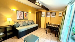 A cozy living room with a sofa, a small table, a dining table, and a balcony with curtains. - House garden garage 10 mn downtown (Nîmes)