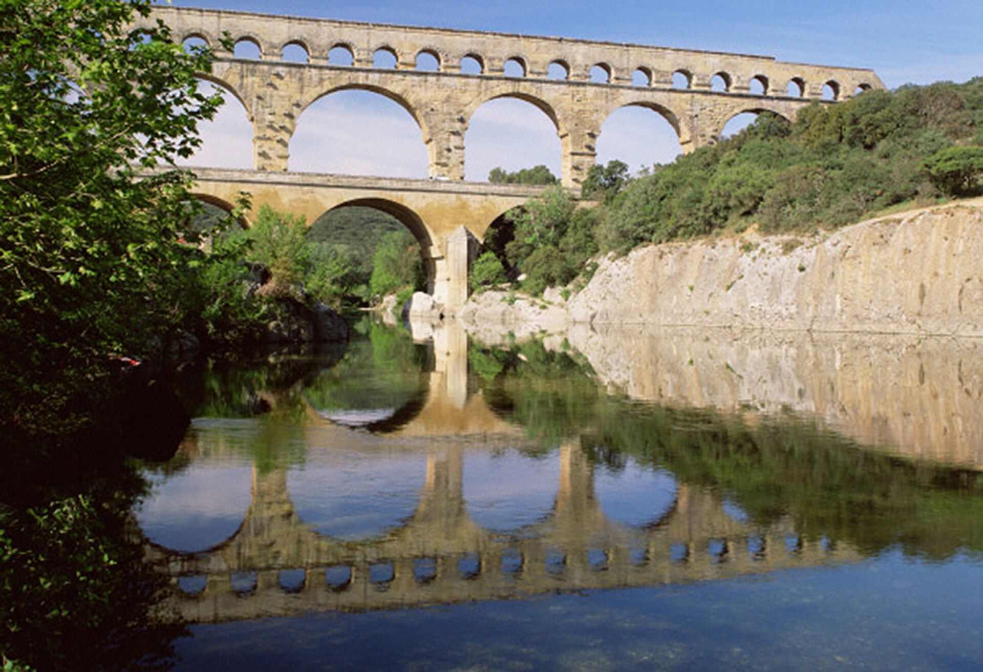 Un puente de piedra con varios arcos sobre un río tranquilo, rodeado de follaje.