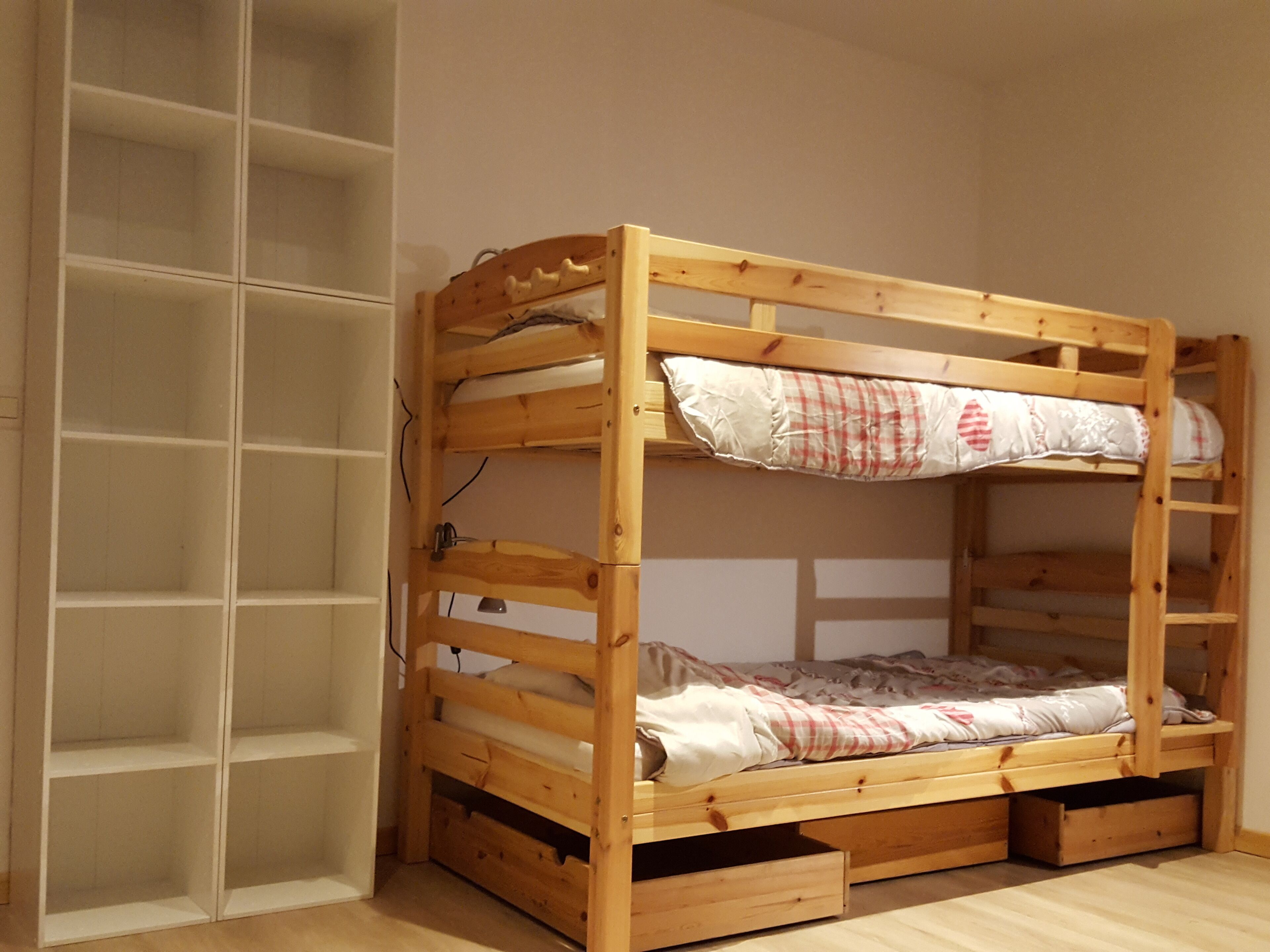 A bunk bed with a wooden frame, a lower shelf, and a storage drawer.