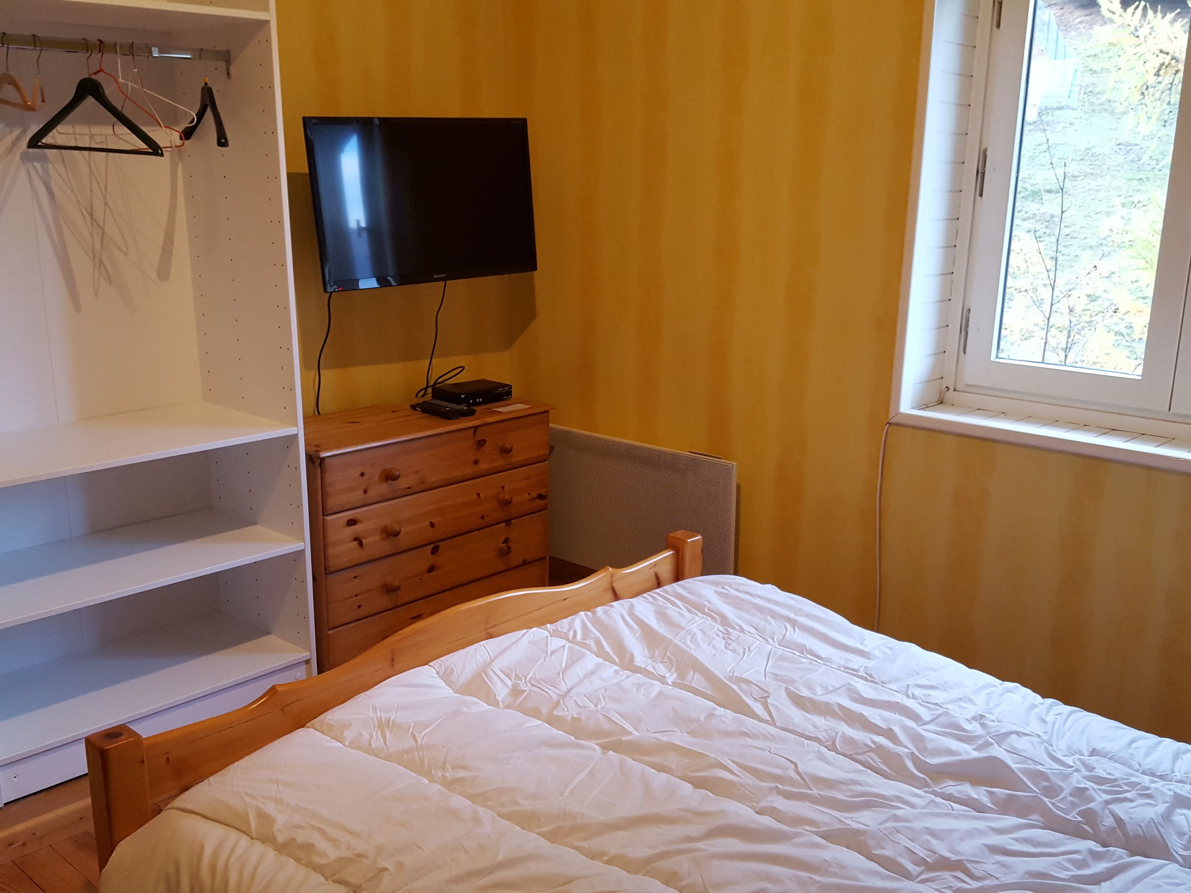Ein Schlafzimmer mit Bett, Schminktisch, Fernseher und Fenster.