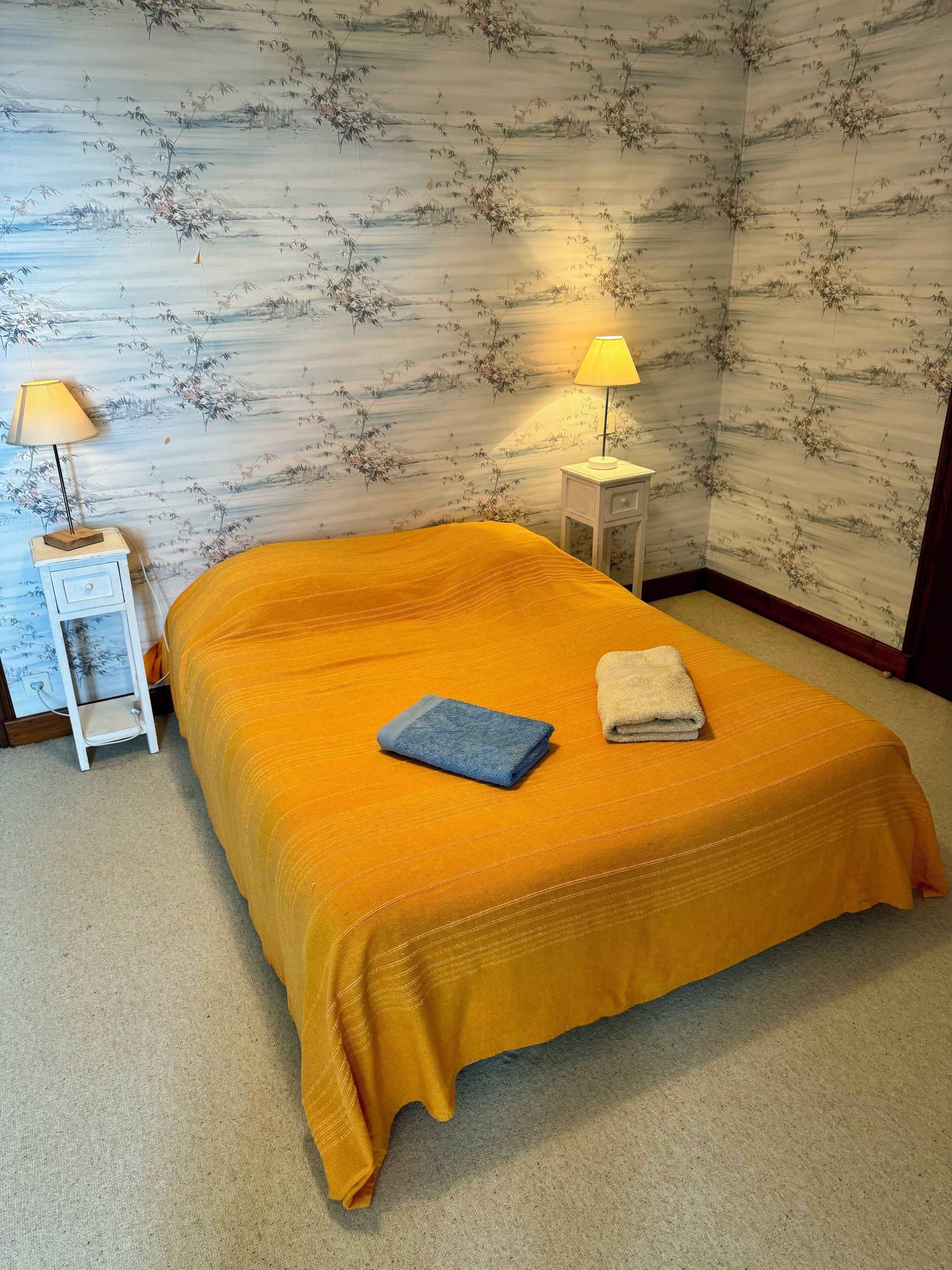 A room with a bed, two bedside lamps, a nightstand, and a wall with a bamboo pattern.