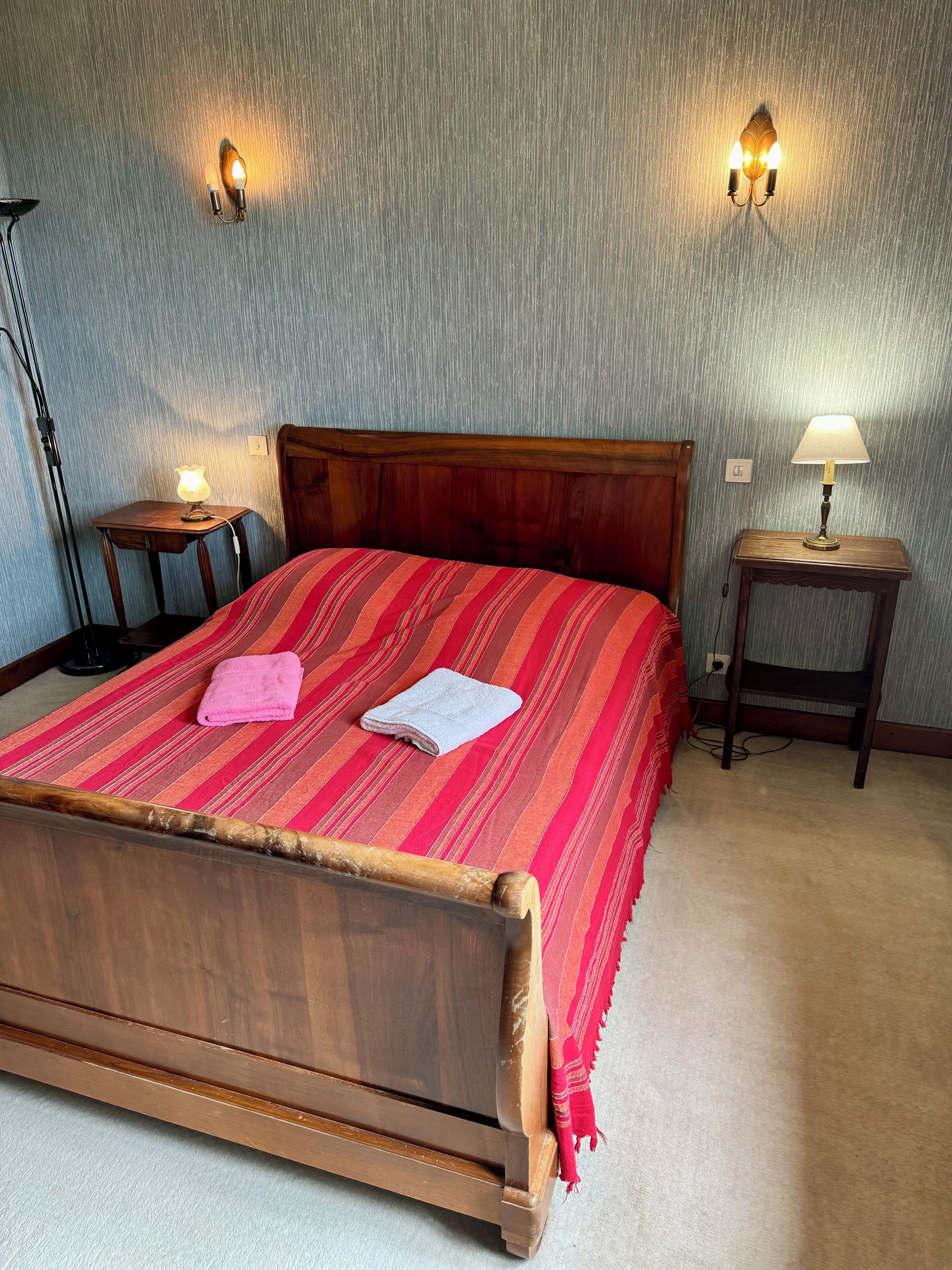 Un lit bien fait, avec une tête de lit en bois, deux lampes de chevet et une petite table sur laquelle se trouve une lampe.