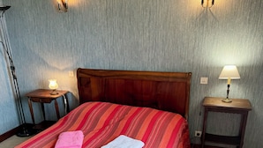 En pænt redt seng med trægavl, to sengeborde med lamper og et lille bord med lampe.