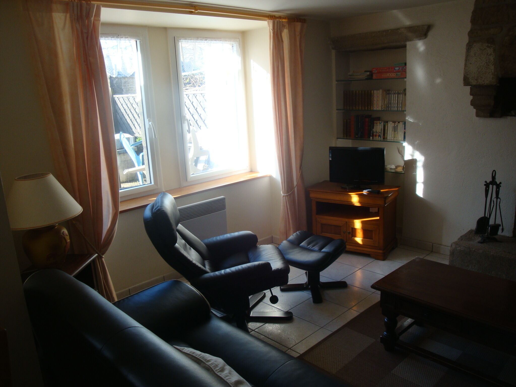 A living room with a sofa, a chair, a small table, a TV on a wooden stand, a bookshelf, and a window with curtains.