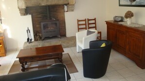 A living room with a stone fireplace, a wooden cabinet, a black armchair, and a white armchair.