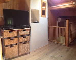 A room with a television on a stand, wicker baskets, a wooden gate, and a white wall.